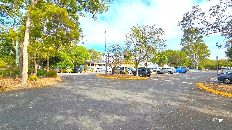 The parking lot at Cleveland Aquatic Centre is a large open space full of varying colors of cars. The garden edges are painted in yellow. White line markings can be seen around the parking lot. Tall trees with great canopy cover provide a calm, environmental feel to the facility.