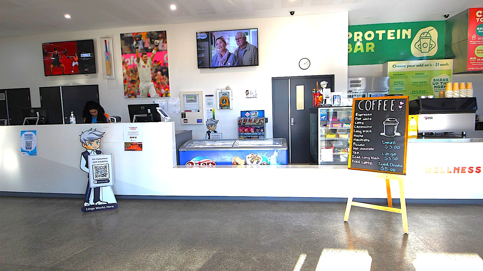 Upon entering the Michael Clarke Recreation Centre, a long, white reception counter with reception staff wearing blue polo shirts along with their warm smiles will greet you upon your arrival. On the left side of the reception desk is the brand icon of Cérge with a QR code for customers with disability. Right next to the reception area is a Café. Different coffee flavors are offered, which guests can choose on the chalkboard menu in front of the desk.