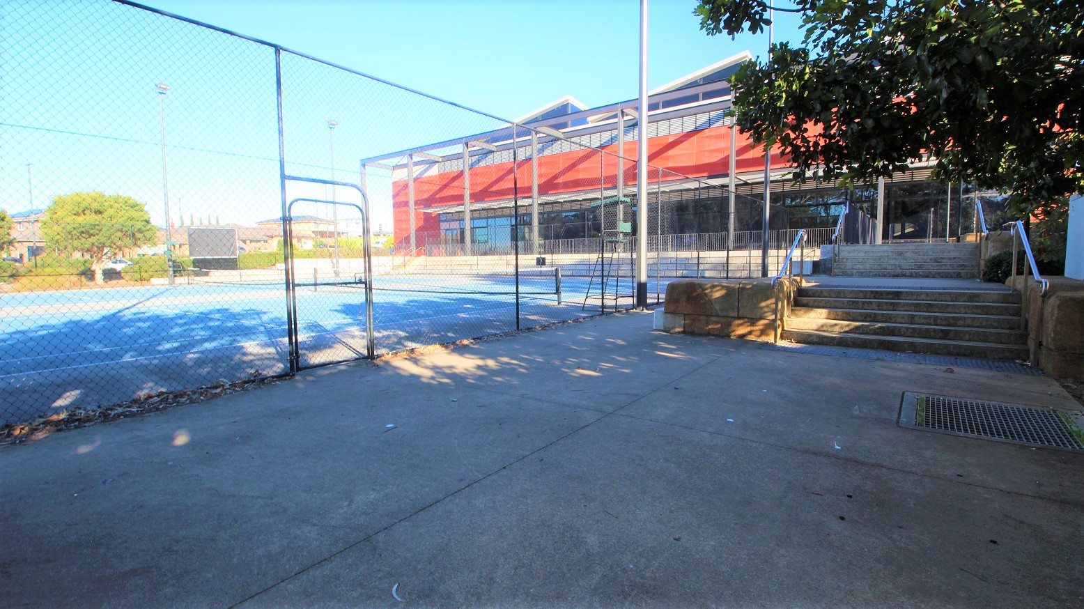 Entrance door to the Tennis Courts at Michael Clarke Recreation Centre. Entry is through the staircase with handrails down the hill from the main entrance of the venue. The shade of trees offers a shield from the sun's direct heat.