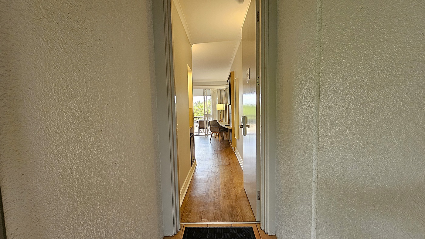 On the left, a grey wall with a small white wall light. To the right, another grey wall with a similar white wall light and a fire extinguisher cabinet. In the middle, two grey doors numbered 319 and 318, each with a black doormat in front. The floor is tiled in light brown, and the ceiling is white with a small recessed light and ventilation grilles.