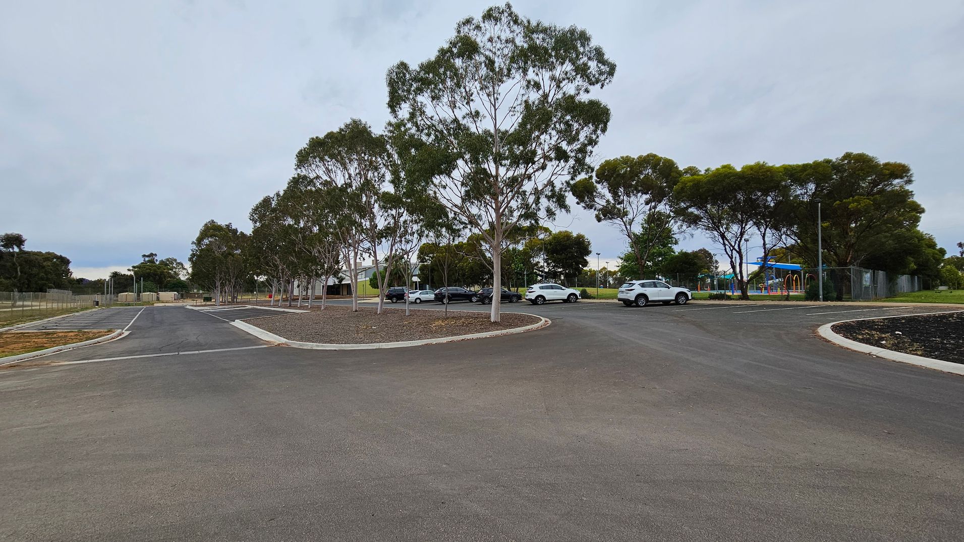 A paved road curves to the left, lined with trees and parked cars. On the right, a blue sign reads "Robinvale Recreation & Aquatic Centre" with amenities listed. A footpath runs parallel to the road, bordered by grass. In the background, more trees and a few buildings are visible.