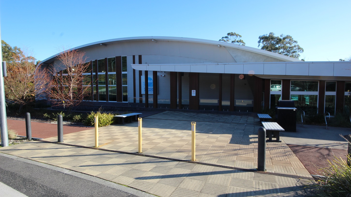There are designated accessible car spaces located near the entrance of Splash Devonport. These spaces are marked with yellow bollards and yellow lines to indicate that they are reserved for persons with disabilities. Surrounding the car spaces is a pathway to move around the whole venue. On the curbs of the parking area is a plant box with a tree, while others have shrubs with moderate leaf length.