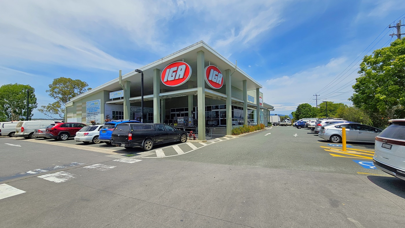 Accessible parking spaces in front and the right side of the nearby road. Cars are visibly parked in an organized manner. On the right, a road pole with lines in yellow hues separates two accessible car parking spaces.. Two huge IGA logos are visibly placed above the entrance of the building.