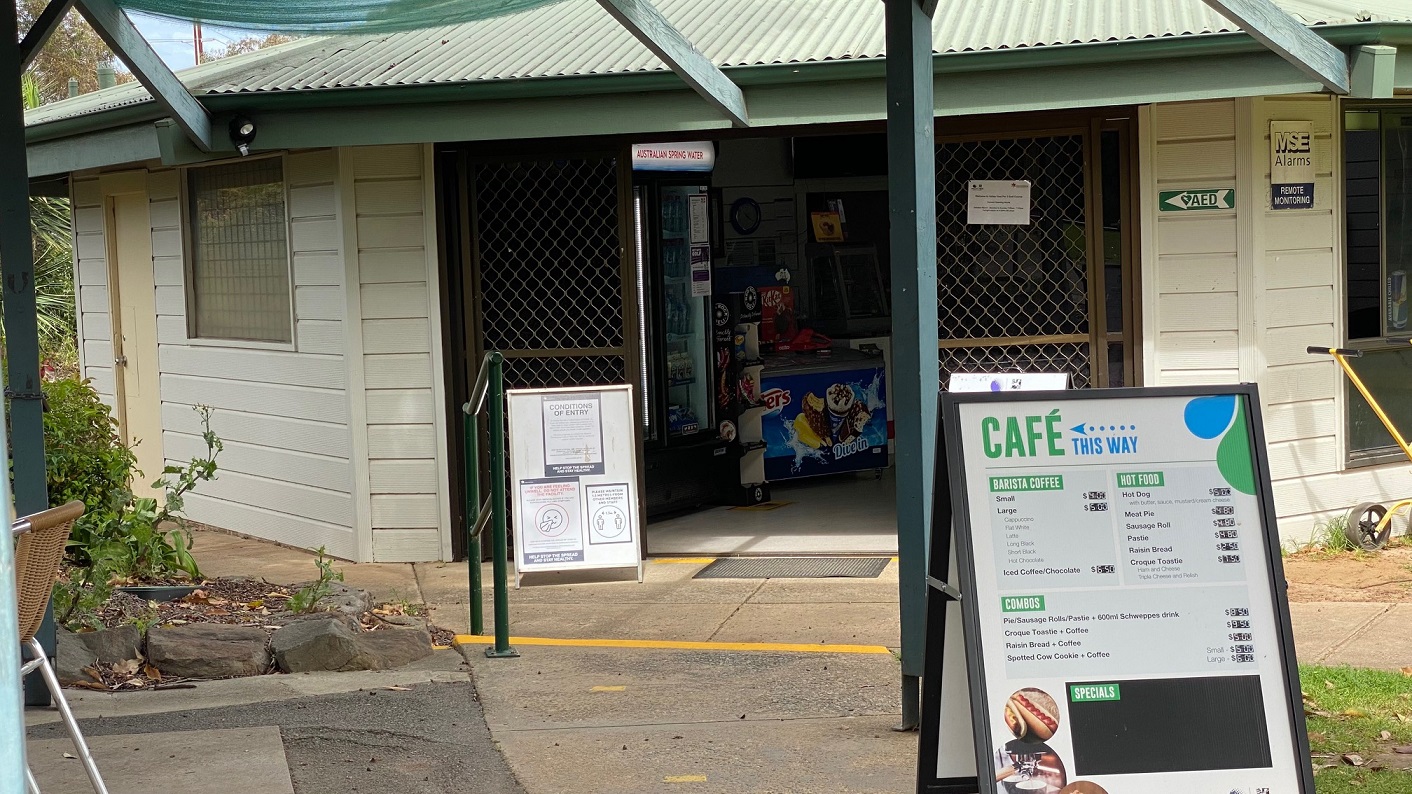 The clubhouse is accessed through a large sliding door, has two notice boards positioned outside and a green handrail is next to the steps. An ice cream freezer is just inside the entrance.