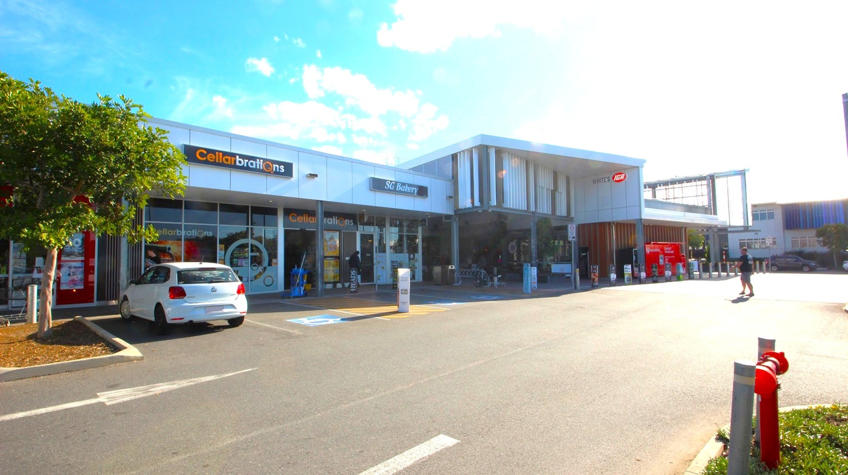 Driveway and accessible parking bays close to White’s IGA Baringa. Close to the image view is the metal bollards with triangular marketing promotions of White’s IGA which can also be found on the edge of the pathway connected to the entrance and to the other shops. There are accessible parking bays on the left side, in front of SG Bakery and Cellarbrations, which can be identified by the accessible parking sign as well as the yellow lines painted on the floor.
