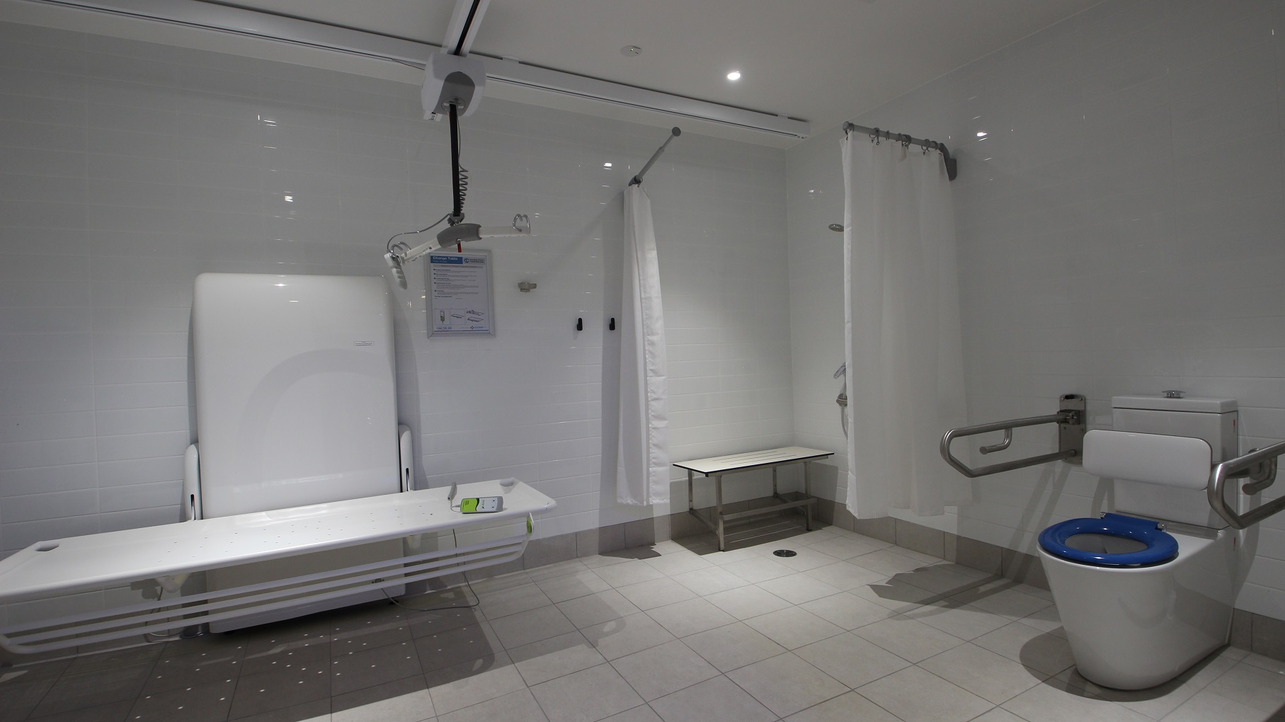 The toilet inside the Aquatic Centre section has different sections. There is a shower section that has movable white curtains. You will also find a wall support and frame to allow the toilet bed to be electrically raised and lowered at different heights. The white bed base can also be hinged up to be flat against the support as well. An instruction on how to use the white toilet bed equipment is posted on the wall to guide users.