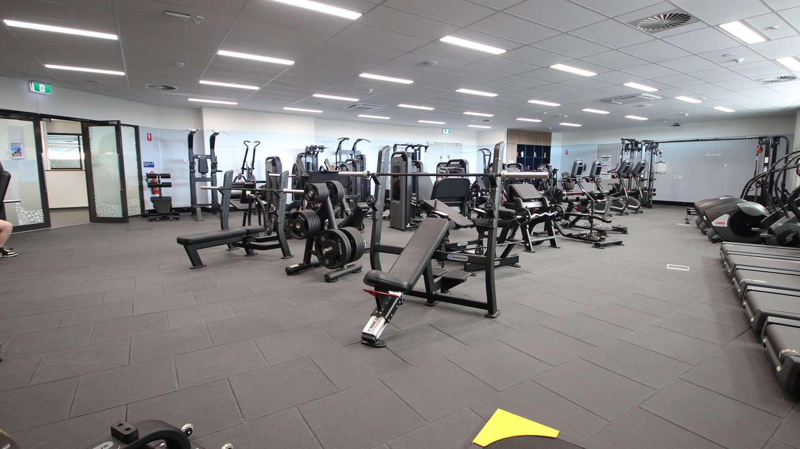 It’s the other side of the fitness room where you will see the glass doors from far left and different fitness equipment occupying most of the floor. The lighting is optimized in every area of the club, which promotes a vibrant and high level of energy. Open and lockers with doors are available at the end corner of the gym. The room has a minimalistic theme because of its white, grey and black colors used.